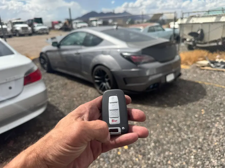 Hand holding a smart proximity key beside a gray coupe on a gravel lot